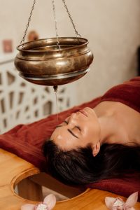 Exploring The Ayurvedic Approach To Pain Management - The Ayurvedic Clinic Relaxed Young Woman Lying Under Shirodhara Vessel During Ayurvedic Procedure